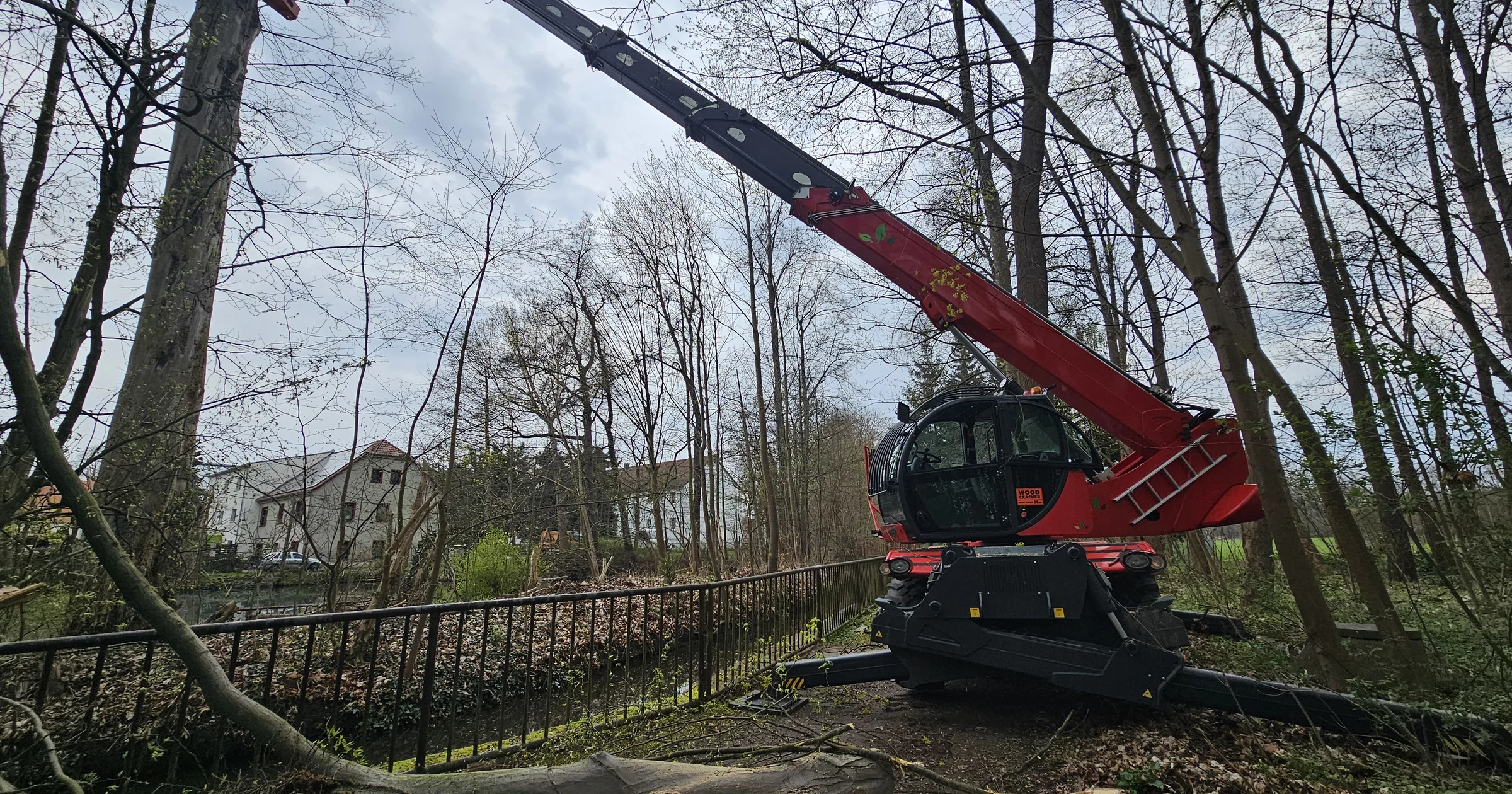 Teleskop-Fällkran bei der Baumfällung, gefälltes Holz im Vordergrund